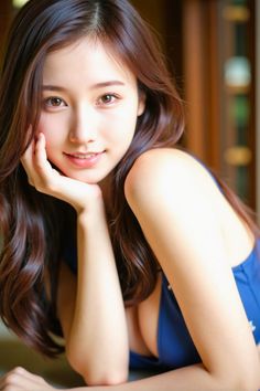 Woman with long brown hair in a blue top, resting her chin on her hand