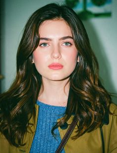 Woman with long wavy hair and green eyes wearing a blue sweater and brown jacket