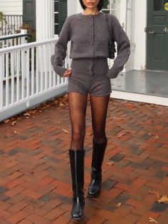 Woman in a gray cardigan and shorts with polka dot tights and black boots outdoors