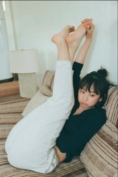 Woman in a black top and light pants lying on a couch with legs raised