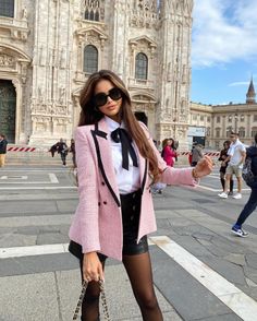 Woman in a pink blazer and sunglasses posing outdoors in a city