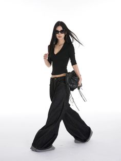 Woman with long black hair and sunglasses wearing a black top and wide leg jeans