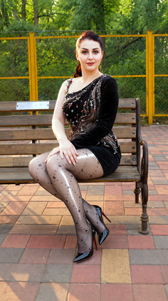 Woman in a black dress and patterned stockings sitting on a park bench