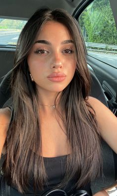 Woman with long dark hair wearing a black top and jewelry in a car