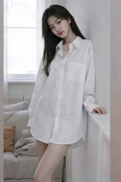 Woman in an oversized white shirt leaning against a wall indoors