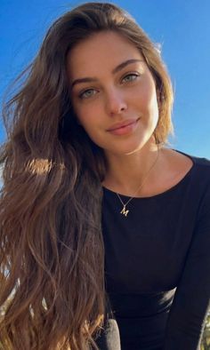 Woman with long brown hair and green eyes wearing a black shirt and gold necklace