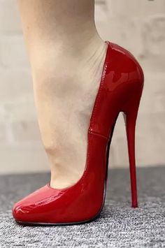 Foot in a red patent leather stiletto high heel shoe on a grey carpet