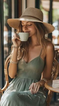 Woman in a straw hat and green dress sipping from a coffee cup at an outdoor cafe