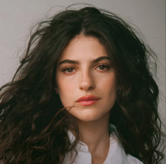 Woman with long, dark, curly hair wearing a white shirt