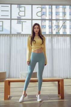 Woman in a yellow crop top and blue leggings standing indoors