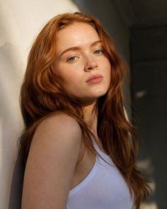 Woman with red hair and blue eyes in a white tank top, lit by soft warm light