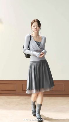 Woman in a light gray long sleeve top and a dark gray midi skirt indoors