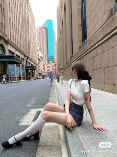 Woman in a white crop top and mini skirt sitting on a city street curb
