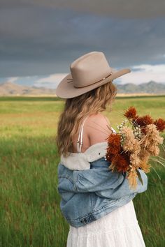 Woman in a cowboy hat and denim jacket holding a bouquet in a green field