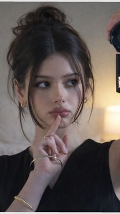 Woman with dark hair in a messy bun, wearing gold jewelry, looking to the side