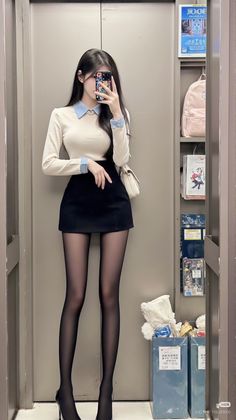 Woman in a white top, black mini skirt, and tights taking a mirror selfie