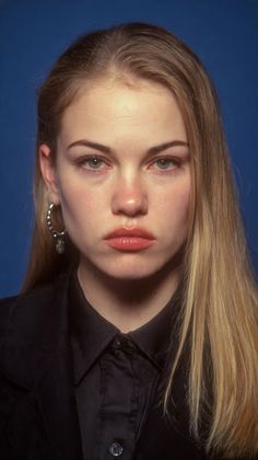 Woman with long blonde hair and a black shirt against a blue background
