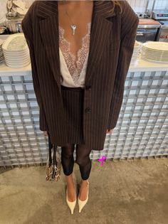 Person in a pinstripe suit with a lace top and key necklace, holding a snakeskin bag