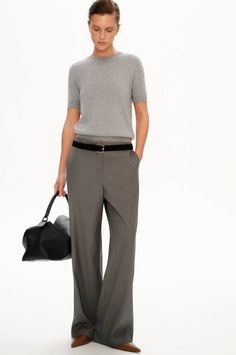 Woman in a gray t-shirt and wide leg pants holding a black handbag
