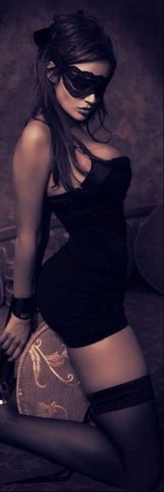 Woman in a black dress and lace mask posing indoors