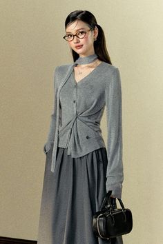 Woman in a gray cardigan and midi skirt holding a black handbag
