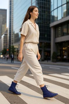 Woman in a beige jumpsuit and blue boots walking across a crosswalk in a city