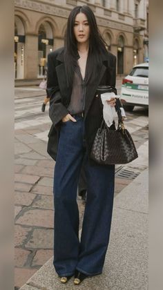 Woman with long black hair wearing an oversized blazer and wide leg jeans on a street