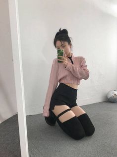 Woman in a pink crop top and black shorts taking a mirror selfie