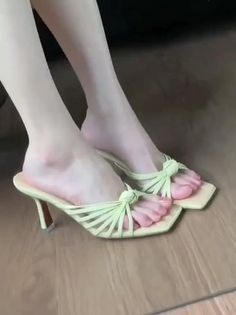 Feet wearing light green strappy high heels on a wooden floor