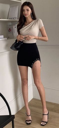 Woman in a black mini skirt with a high slit and a beige top indoors