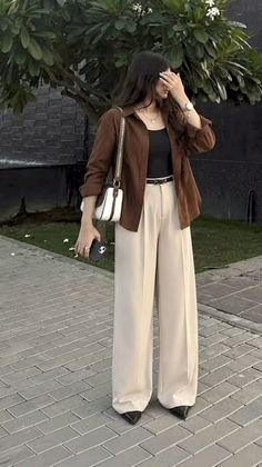 Woman in a brown shirt and wide leg pants holding a phone outdoors