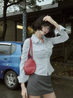 Woman with short hair and glasses wearing a white shirt and mini skirt outdoors