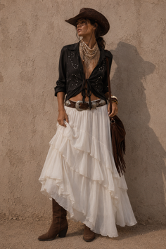 Woman in a cowboy hat, black shirt, and long white skirt with a fringe bag