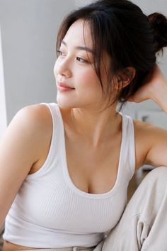 Woman in a white tank top with dark hair in an updo looking away