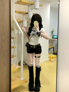 Person with long black hair in a cropped t-shirt and black shorts taking a mirror selfie