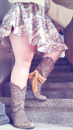 Person in a floral skirt and cowboy boots walking up carpeted stairs