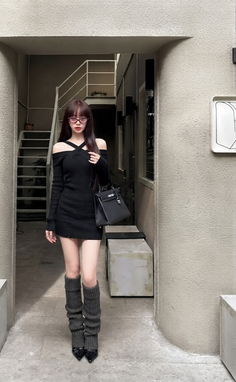 Woman in a black dress, leg warmers, and glasses standing outdoors