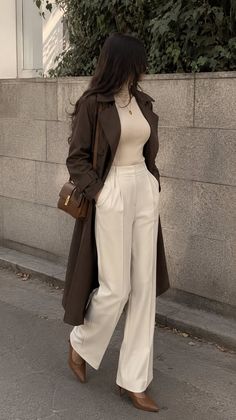 Woman in a brown trench coat and white wide-leg pants walking on a street