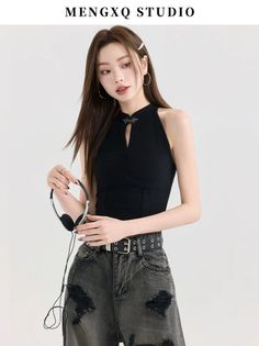Woman with long hair wearing a black halter top and ripped jeans, holding headphones