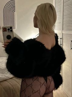 Woman with blonde hair in a fur jacket and fishnet stockings taking a mirror selfie