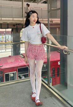 Woman in a white crop top and red gingham shorts with white lace tights outdoors
