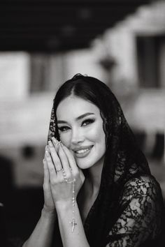 Woman in a lace veil holding a rosary with hands clasped in prayer