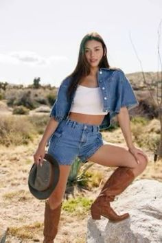 Woman in denim shorts and cowboy boots posing in a desert landscape