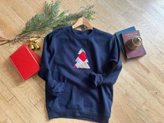 Navy blue sweatshirt with a Christmas tree applique on a wooden floor with holiday decor