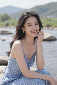 Woman in a blue floral dress smiling by a river with mountains in the background
