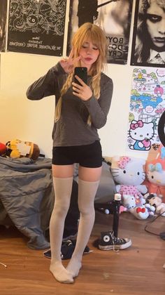 Blonde woman with braids and bangs taking a mirror selfie in a messy room