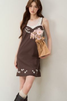 Woman in a brown dress with floral embroidery holding a paper bag of pink flowers