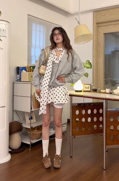 Woman in a polka dot dress and grey cardigan standing indoors