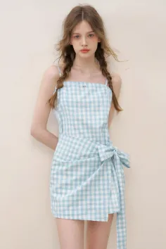 Woman in a light blue gingham dress with braided hair against a plain background