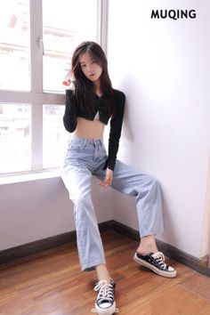 Woman with long hair wearing a crop top and jeans, sitting by a window